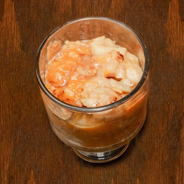 A glass of Dad's BBQ Next Generation peach cobbler on a dark wooden table.