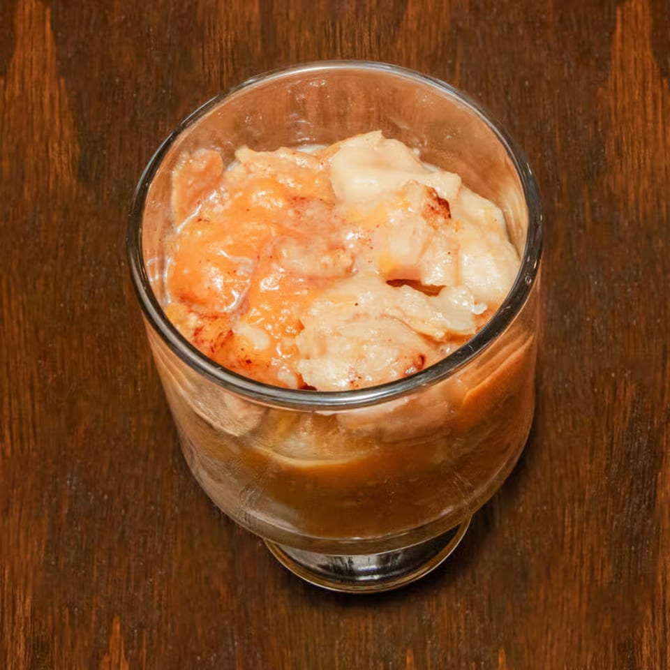 A glass of Dad's BBQ Next Generation peach cobbler on a dark wooden table.