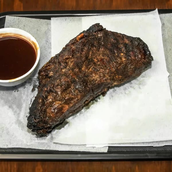 A large, dark, smoked brisket with a side of barbecue sauce on a tray.