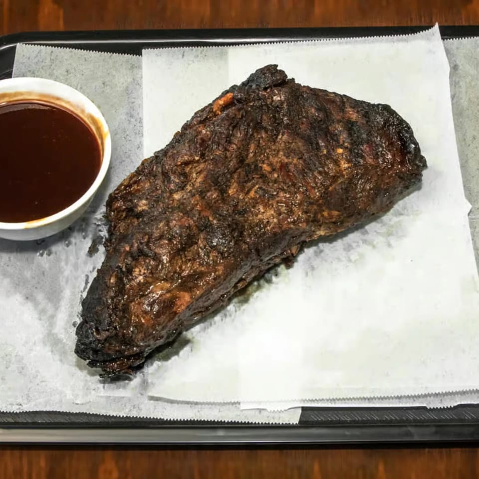 A large, dark, smoked brisket with a side of barbecue sauce on a tray.