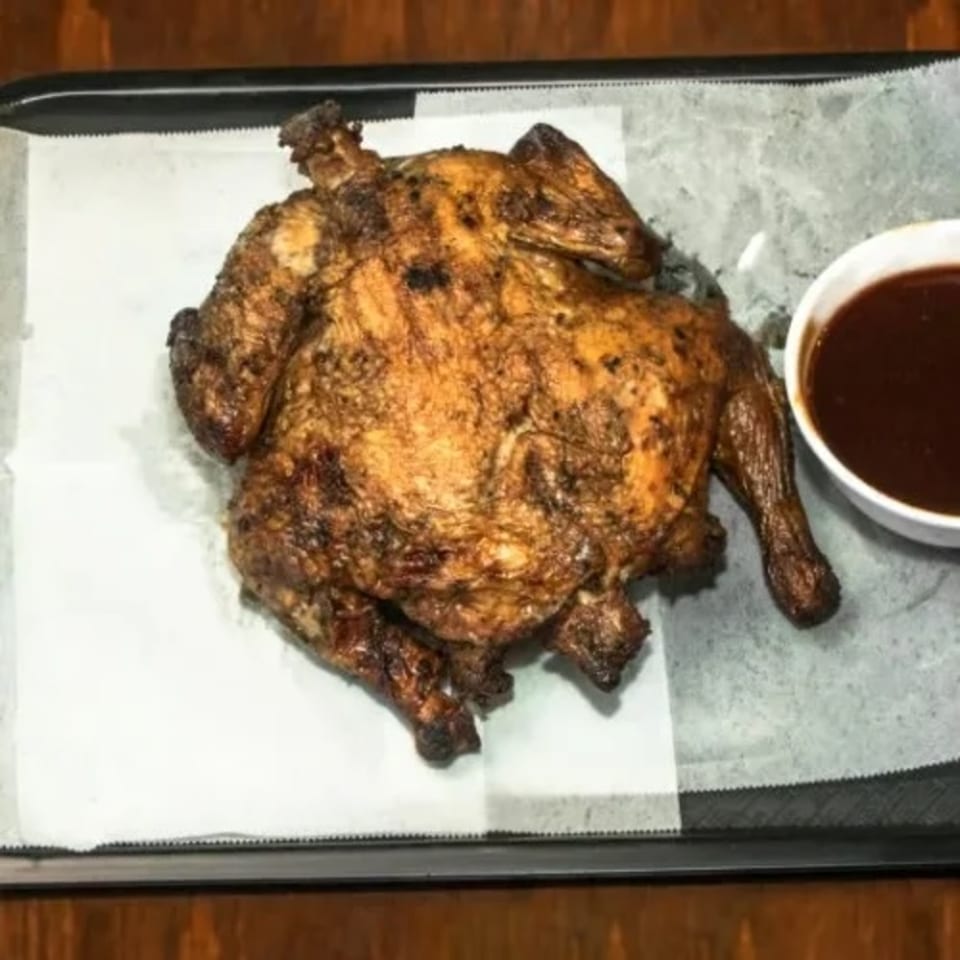 A whole roasted chicken with crispy skin and a side of Dad's BBQ sauce on a tray.