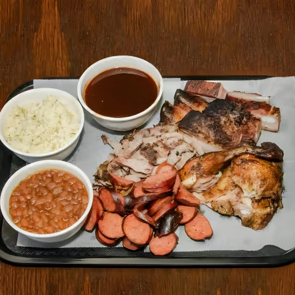 Dad's BBQ platter with sliced chicken, sausage, ribs, baked beans, coleslaw, and BBQ sauce.