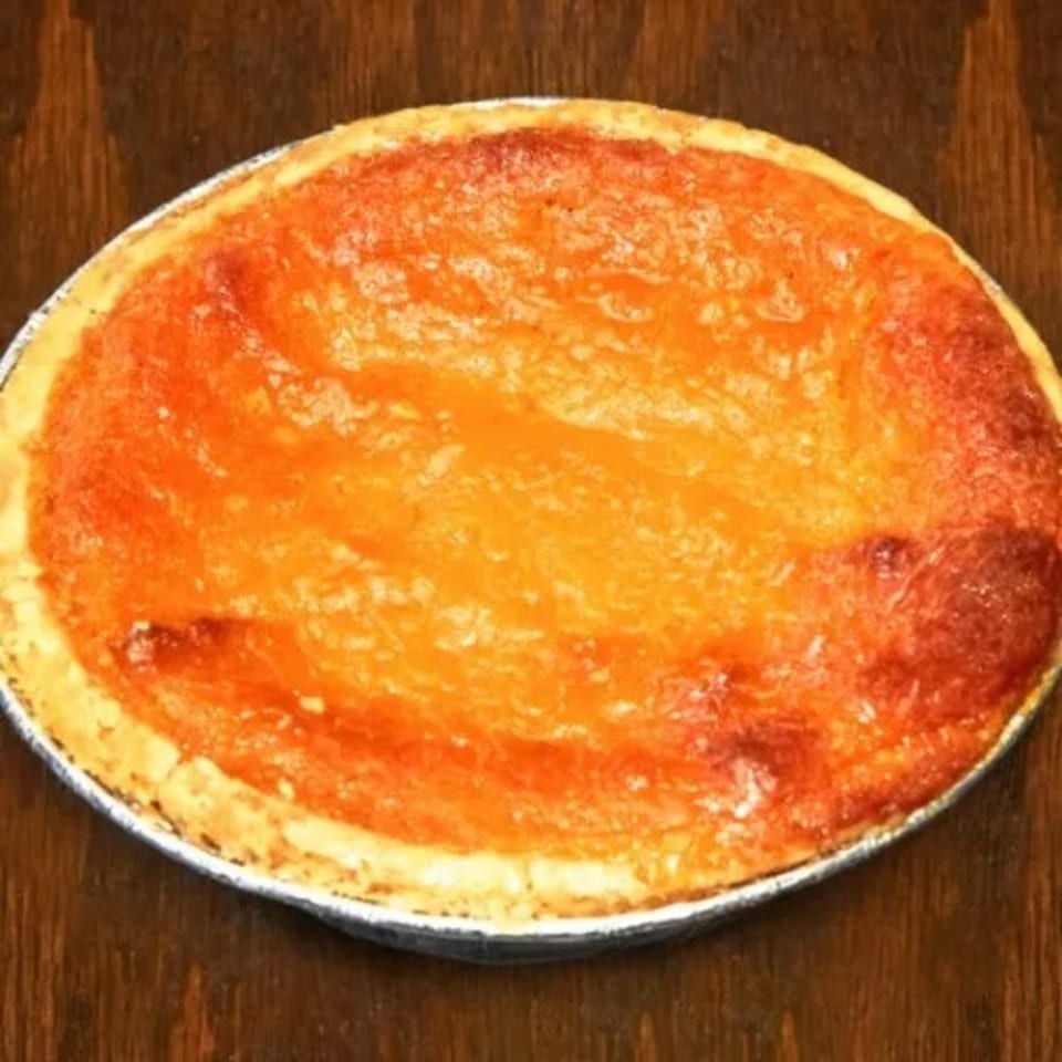 A whole, baked sweet potato pie in a foil pan on a wooden surface.