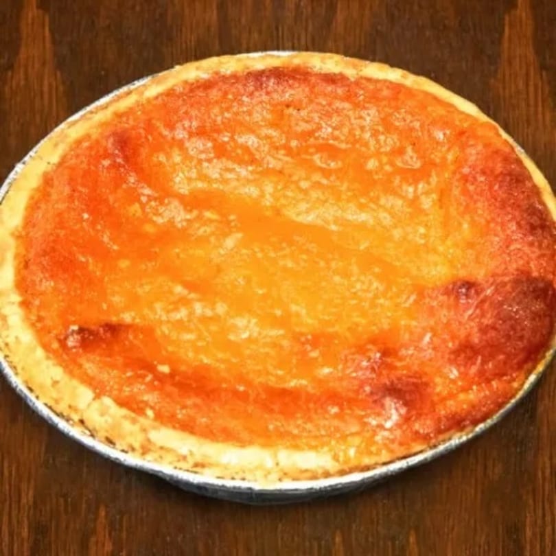 A whole, baked sweet potato pie in a foil pan on a wooden surface.