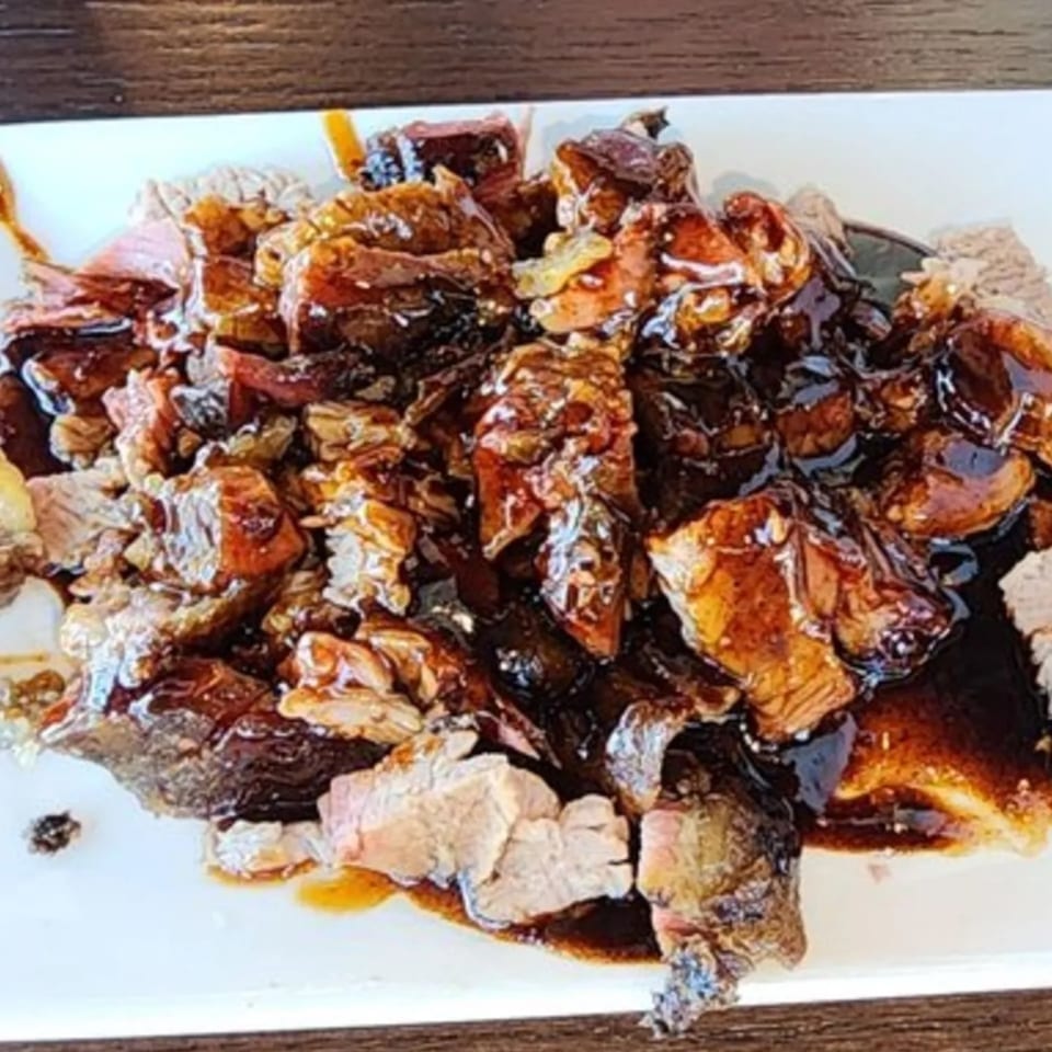 Close-up of Dad's BBQ brisket burnt ends, glistening with rich, dark barbecue sauce on a white plate.